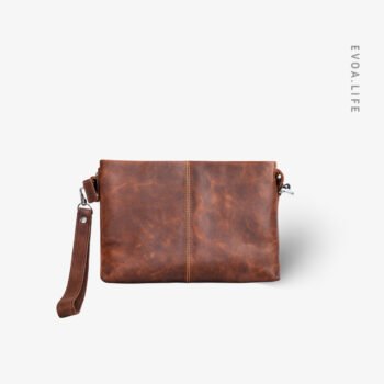 Made in Bangladesh, this rich tan genuine leather clutch bags features a compact silhouette. It offers a structured main compartment designed to neatly organize your essentials like a phone, wallet, & keys without the bulk. With its refined chain strap for shoulder or crossbody wear, this timeless piece transitions effortlessly from work and studies to travel. Its minimal branding & handcrafted finish ensure an elegant look for any occasion.