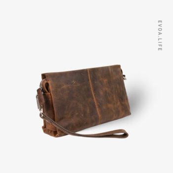 Made in Bangladesh, this rich tan genuine leather clutch bags features a compact silhouette. It offers a structured main compartment designed to neatly organize your essentials like a phone, wallet, & keys without the bulk. With its refined chain strap for shoulder or crossbody wear, this timeless piece transitions effortlessly from work and studies to travel. Its minimal branding & handcrafted finish ensure an elegant look for any occasion.